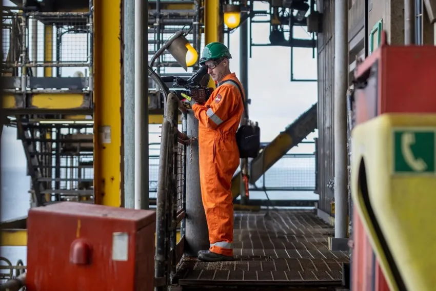 Elliot Hornell operating a camera in orange coveralls on an offshore installation