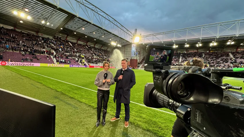 Broadcast camera filming a presenter and guest pitchside at an evening football match